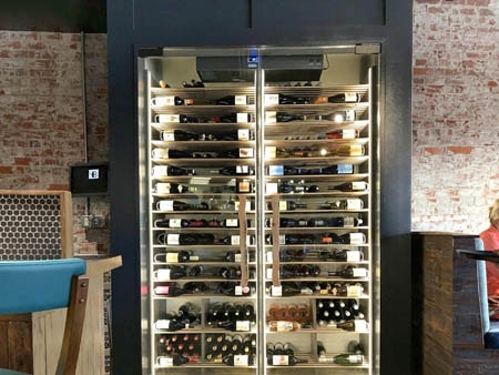 Impressive black trimmed glass wine cabinet inside a bustling restaurant.