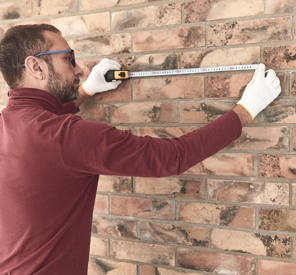 Man measuring a brick wall for cellar installation